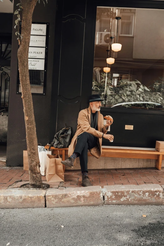 a man sitting on a bench next to a tree, trending on pexels, bakery, wearing trenchcoat, sydney, shop front