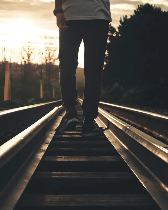 someone standing on railroad tracks near the sun