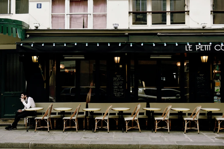 a man sitting at a table outside of a restaurant, by Raphaël Collin, unsplash, art nouveau, awnings, ignant, french kiss, empty stools