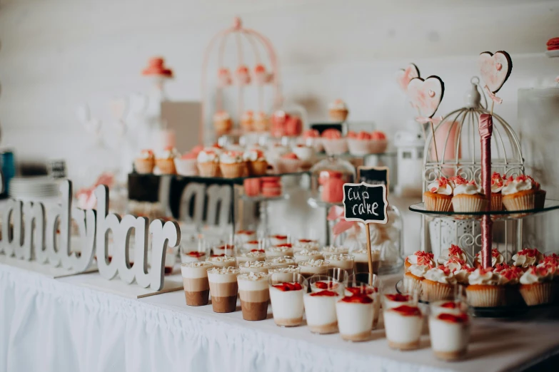 a table topped with lots of cupcakes and desserts, a picture, by Emma Andijewska, unsplash, in white lettering, light red and orange mood, square, low quality photo