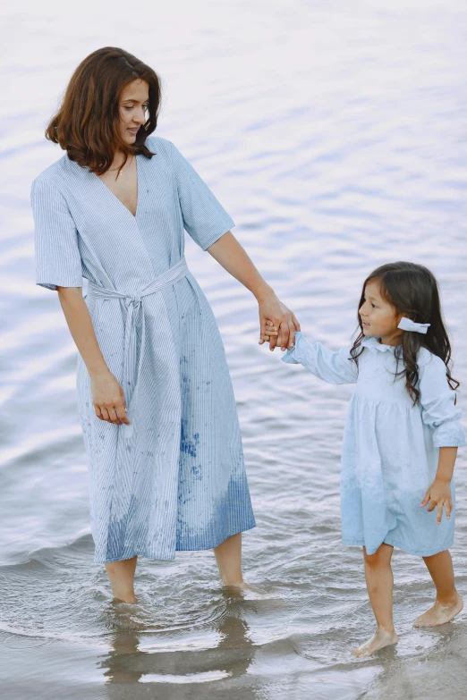 a woman and a little girl standing in the water, inspired by Cui Bai, unsplash, conceptual art, pale blue outfit, in a beachfront environment, water stains, robe