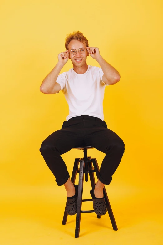 the man is sitting on top of a stool with his hands up