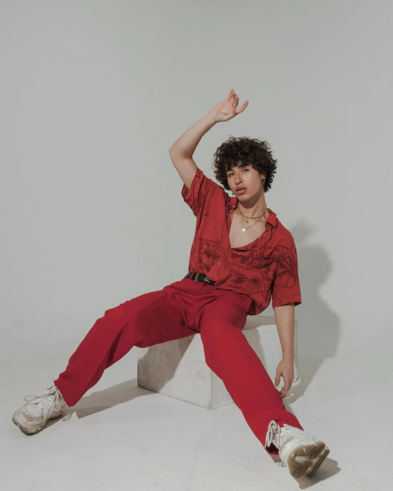 a man in a red shirt and red pants, an album cover, trending on pexels, non binary model, sitting pose, curly haired, triumphant pose
