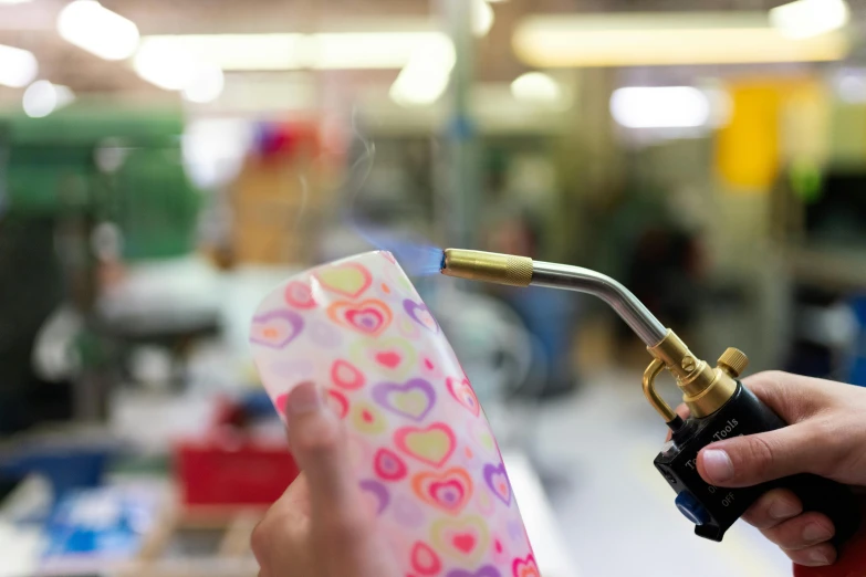 a close up of a person holding a welding torch, an airbrush painting, trending on pexels, sheer fabrics, in a workshop, looking cute, glass and gold pipes