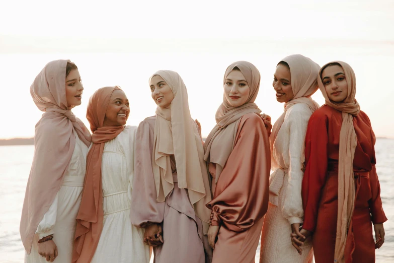 a group of women standing next to each other on a beach, inspired by Maryam Hashemi, trending on pexels, hurufiyya, somali attire, rose tones, south east asian with long, neutral colours