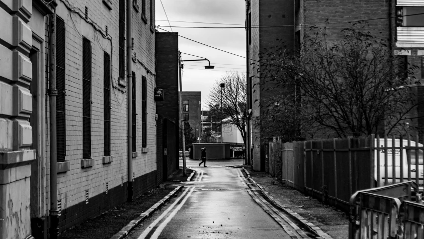 a black and white image of an alleyway and the street is wet