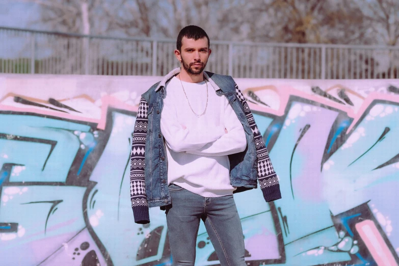 a man wearing jeans and jacket standing in front of graffiti wall