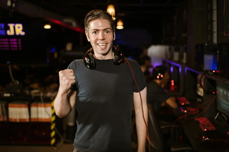 a man in a black shirt holding a pair of headphones, arcade, celebrating, smiling at camera, lane brown