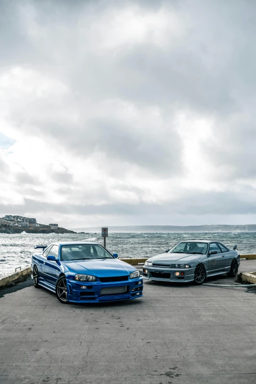 two stance cars parked on a stone lot next to the ocean