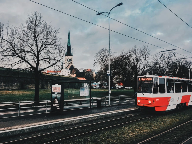 a red and white train traveling down train tracks, by Emma Andijewska, pexels contest winner, viennese actionism, street tram, church in the background, 🚿🗝📝, thumbnail