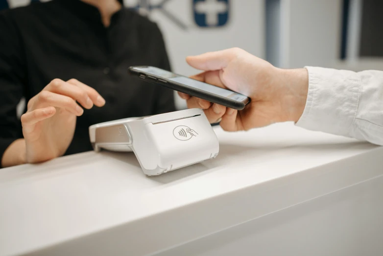 a close up of a person using a cell phone, at checkout, with a white, on a table, a person standing in front of a