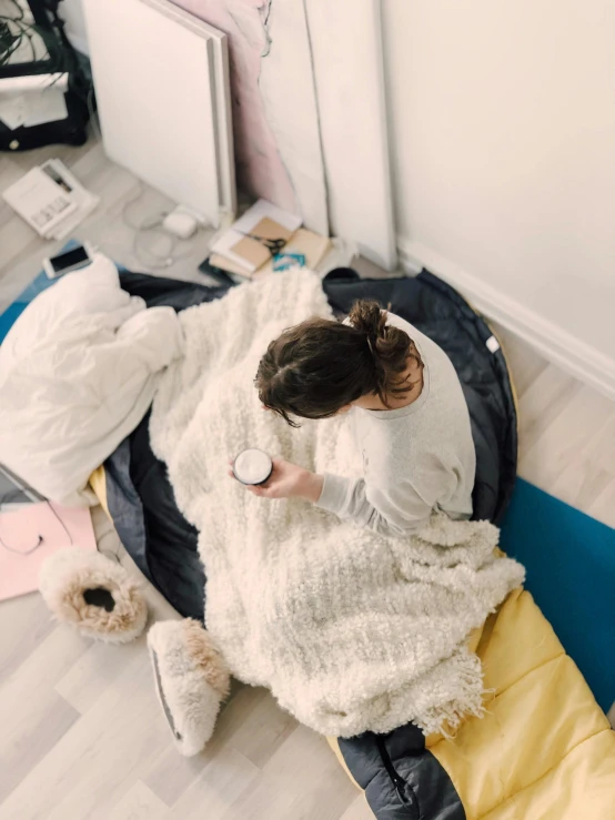 a woman sitting on top of a bed covered in a blanket, trending on pexels, happening, with a bunch of stuff, high angle shot, profile image, carpeted floor