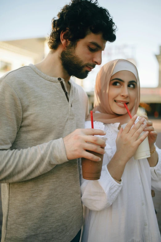 a man and a woman standing next to each other, a picture, trending on pexels, hurufiyya, with a straw, arabic, drink, wearing casual clothes