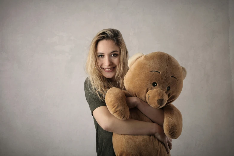 a woman holding a teddy bear in her arms, by Adam Marczyński, pixabay contest winner, photorealism, gigantic titan winnie the pooh, blond, studio shoot, smiling