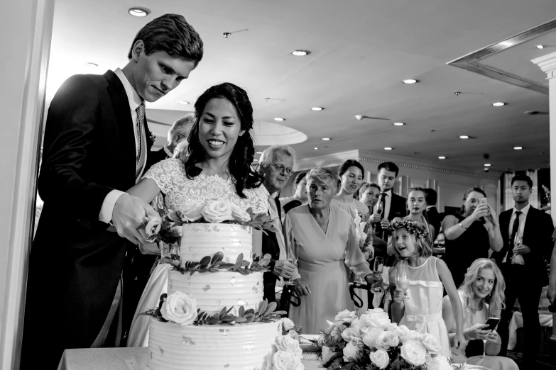 a black and white photo of a bride and groom cutting their wedding cake, by Sam Dillemans, renaissance, multi - level, karla ortiz, beautiful look, happy birthday
