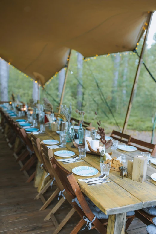 a wooden table with plates and utensils under a tent, forest setting in iceland, amber and blue color scheme, exterior, riding