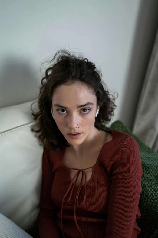 a woman sitting on a couch with a remote in her hand, a character portrait, inspired by Moses Soyer, pexels contest winner, photorealism, suspiria, serious focussed look, curls, daisy ridley