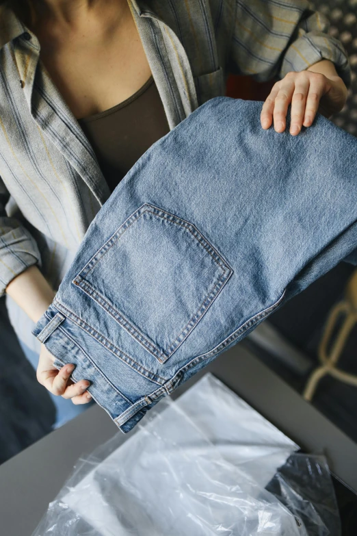 a person standing in front of a table holding up a pair of blue jeans