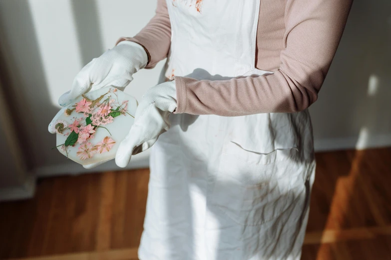 a woman in an apron holding a plate with flowers on it, inspired by Jean-Marc Nattier, pexels contest winner, process art, botanical herbarium paper, white and pink cloth, soap carving, holding controller