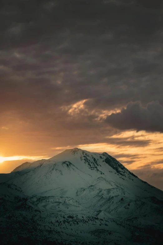 a snowy mountain is silhouetted against a cloud - backed sky