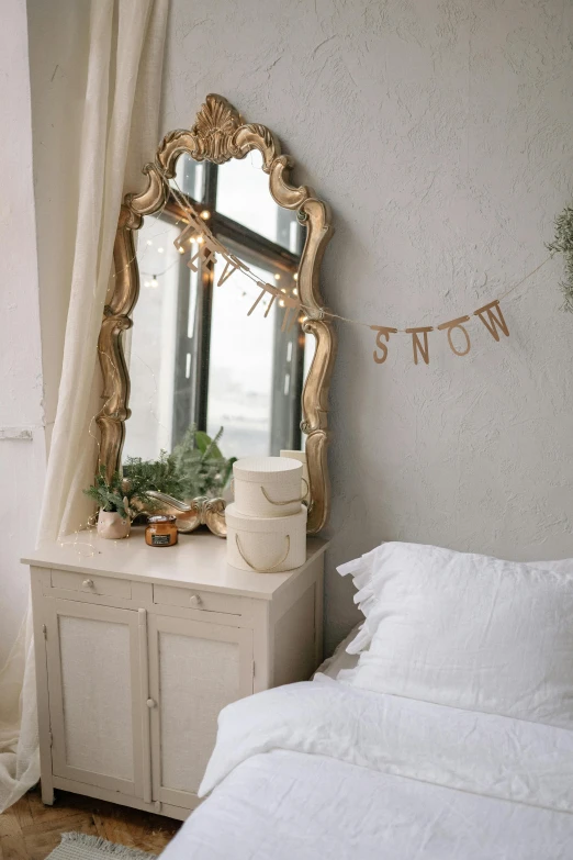 a white bed with pillows, a nightstand with a mirror and plant