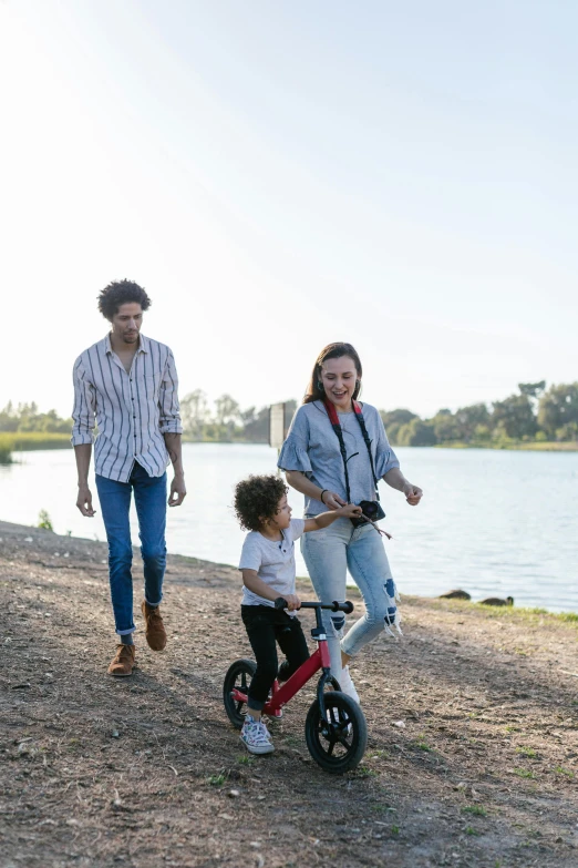 a man riding a scooter next to a woman and a child, near a lake, profile image