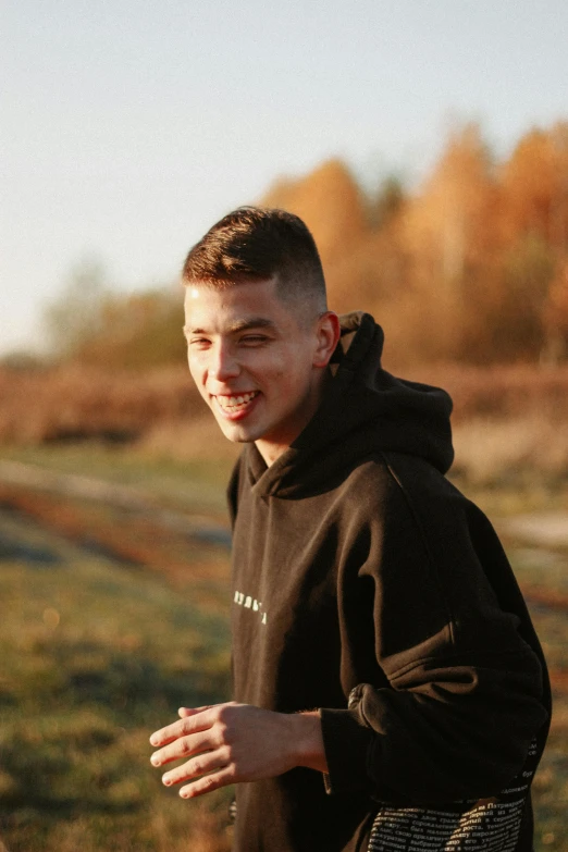 a young man smiling as he stands in the field