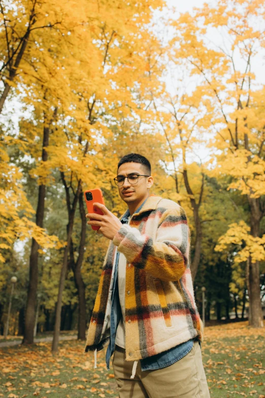 a man standing in a park taking a selfie, trending on pexels, 🍂 cute, li zixin, non-binary, yellow and red