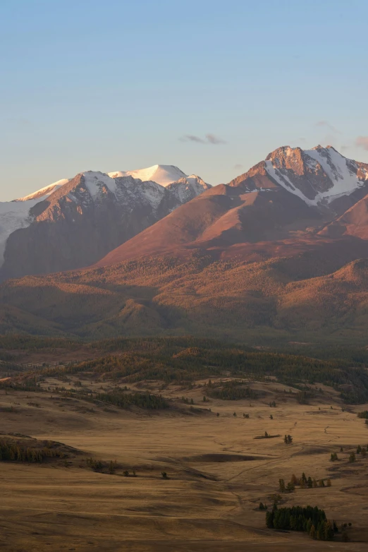 a grassy field covered in snow covered mountains