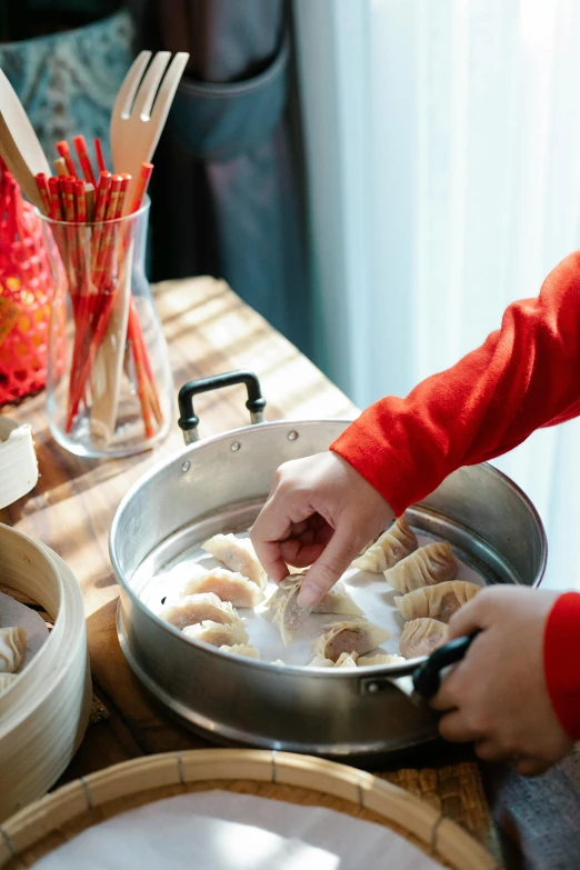 a person in a red shirt preparing food on a table, dumplings on a plate, swirling schools of silver fish, family friendly, holiday season