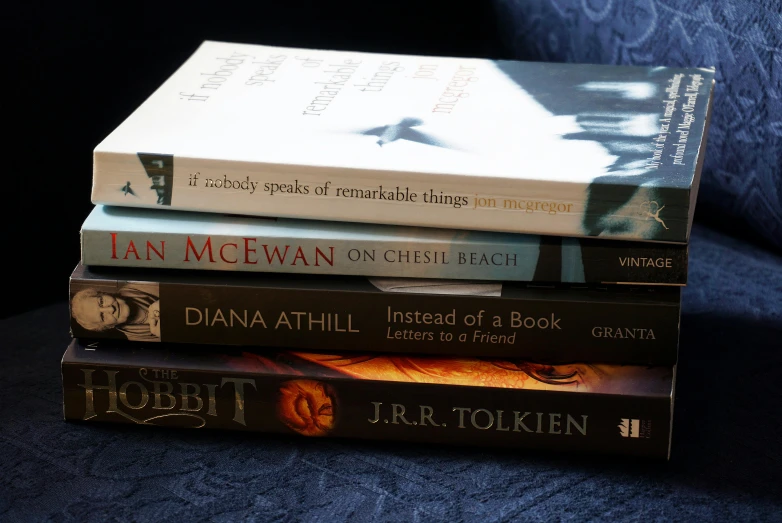 a stack of books sitting on top of a blue couch, a portrait, by David Donaldson, pexels contest winner, renaissance, tolkien, alan lee and marc simonetti, etched inscriptions, on black background