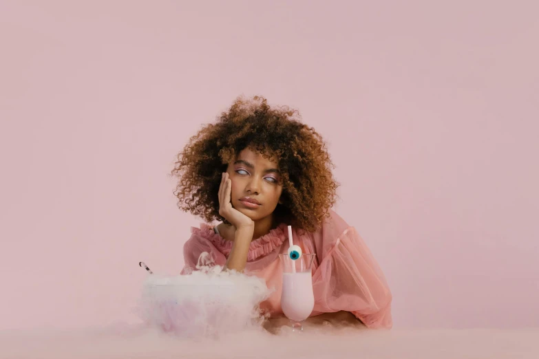woman with curly hair wearing pink sitting on a stool