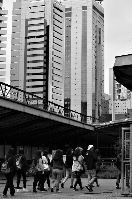 a group of people walking down a street with a train station and building in the background