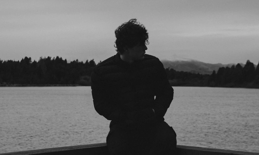 a man standing in front of a body of water, a black and white photo, harry styles, man sitting facing away, profile image, robb stark