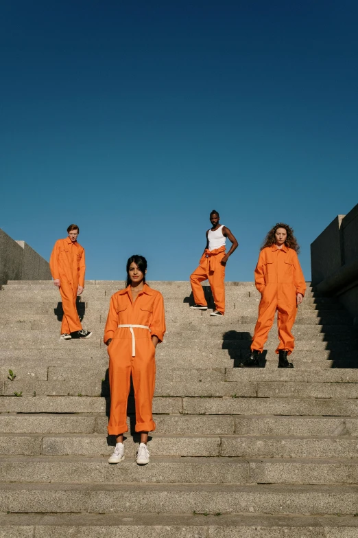 a group of people that are standing on some steps, an album cover, trending on pexels, wearing orange prison jumpsuit, hammershøi, wearing human air force jumpsuit, hila klein