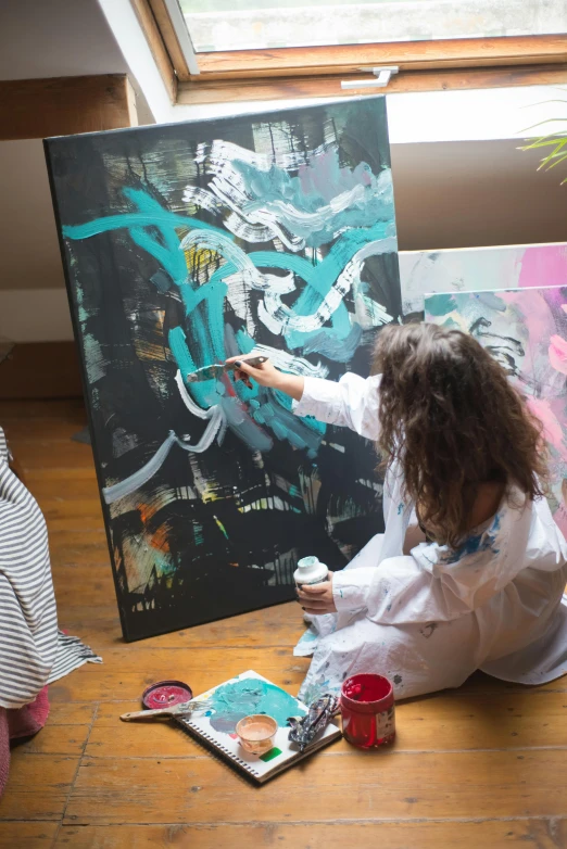 a little girl sitting on the floor in front of a painting, a painting, pexels contest winner, process art, artist wearing overalls, graffiti throws, a painting of two people, painting on black canvas