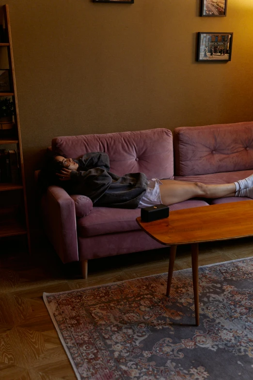 woman lying on pink couch with arms crossed next to wooden table