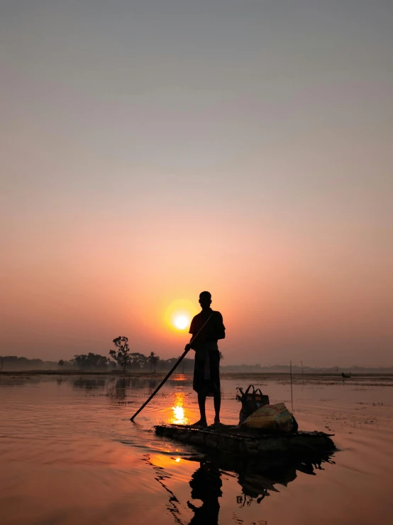 a man standing on top of a boat in the water, by Sunil Das, sunset in the background, assamese, 2022 photograph, lightweight