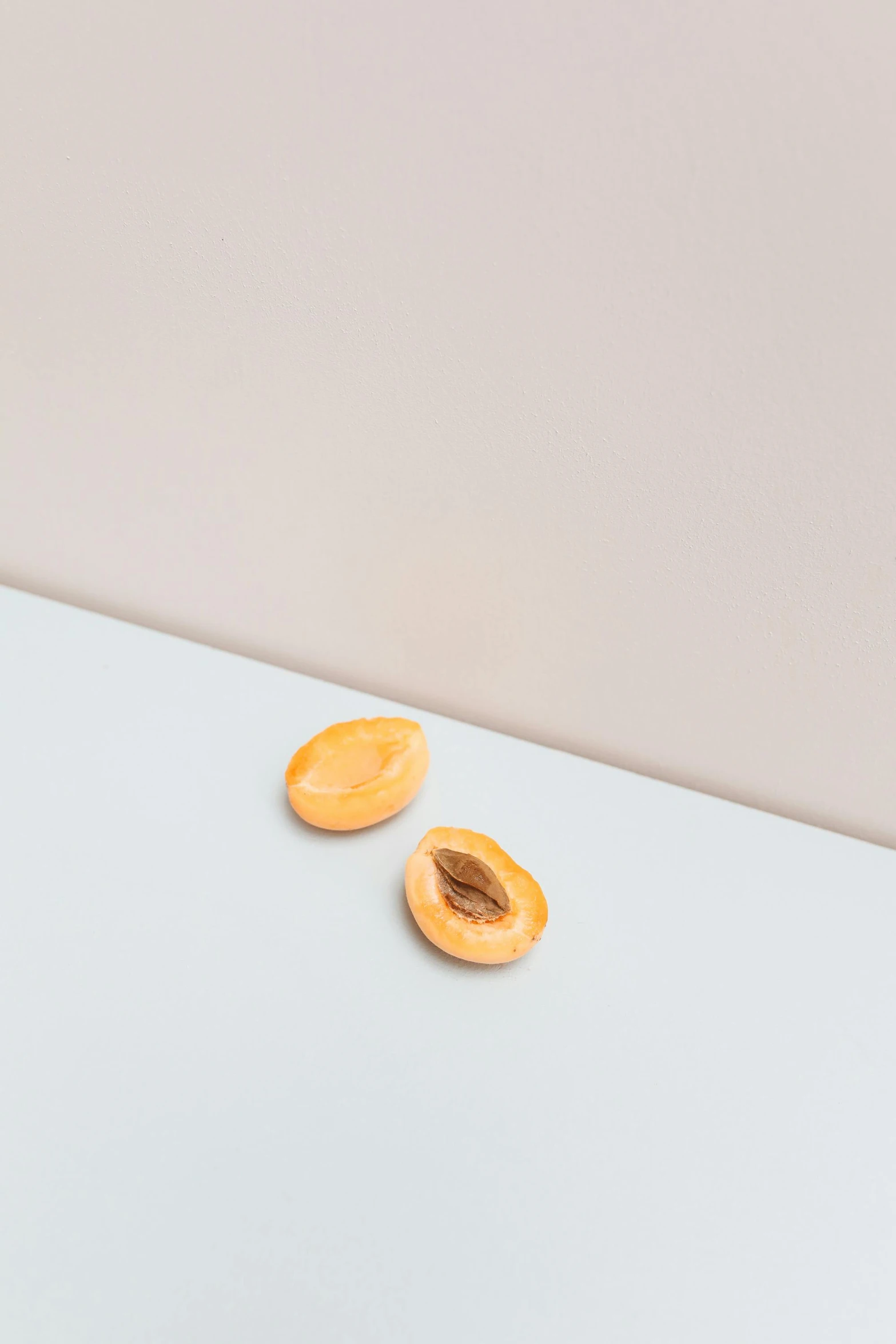 two pieces of apricot sitting on top of a table, by Harvey Quaytman, trending on unsplash, visual art, plain background, with small object details, soft oval face, opening shot