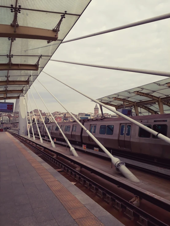 a train pulling into a train station next to a platform, a picture, skyline showing from the windows, canopies, instagram picture, diagonal lines