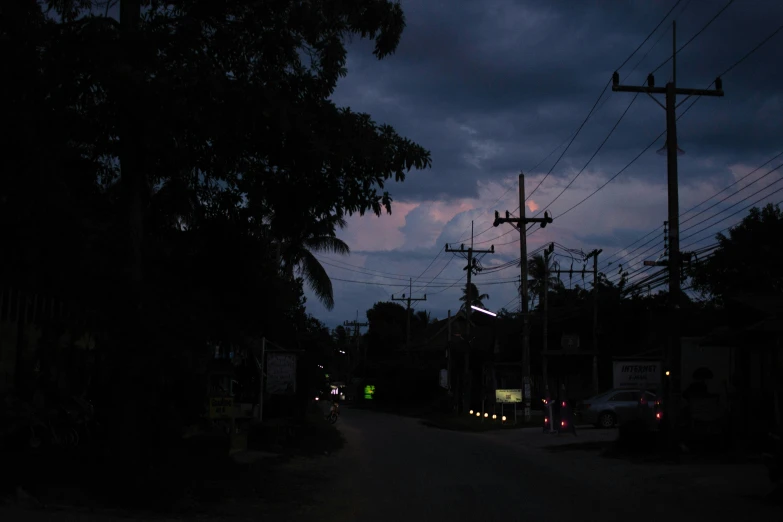 a street filled with lots of traffic under a cloudy sky, an album cover, inspired by Nan Goldin, unsplash, hurufiyya, moonlit kerala village, powerlines, humid evening, nightfall. quiet