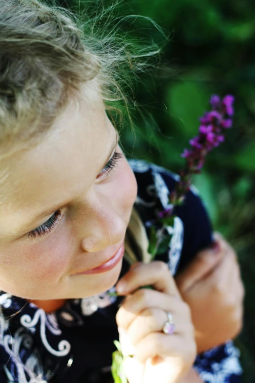 a little girl with a flower in her hand, inspired by Sophie Anderson, unsplash, salvia, zoomed in, portrait of nordic girl, purple