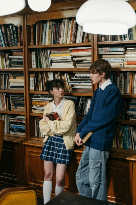 a couple of people standing in front of a bookshelf, an album cover, trending on pexels, paris school, male ulzzang, school uniform, ( ( theatrical ) ), ekaterina