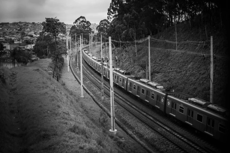 a train traveling down train tracks next to a lush green hillside, a black and white photo, by Alejandro Obregón, unsplash, figuration libre, in sao paulo, machines and wires everywhere, fotografia blanco y negro, in a row