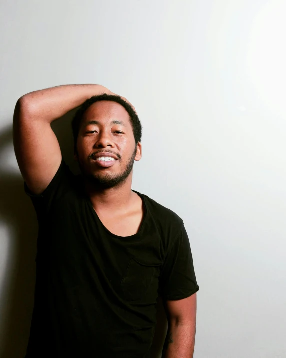 a man wearing a black shirt is leaning against a white wall