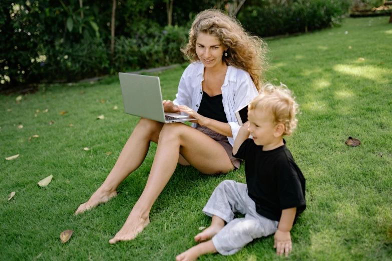 a woman and a child sitting on the grass with a laptop, by Carey Morris, pexels, lush lawn, avatar image, people at work, a blond