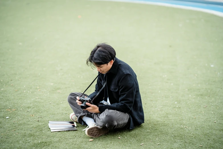 a man sitting on the ground holding a camera, a picture, by Jang Seung-eop, playing games, medium format, student, rectangle