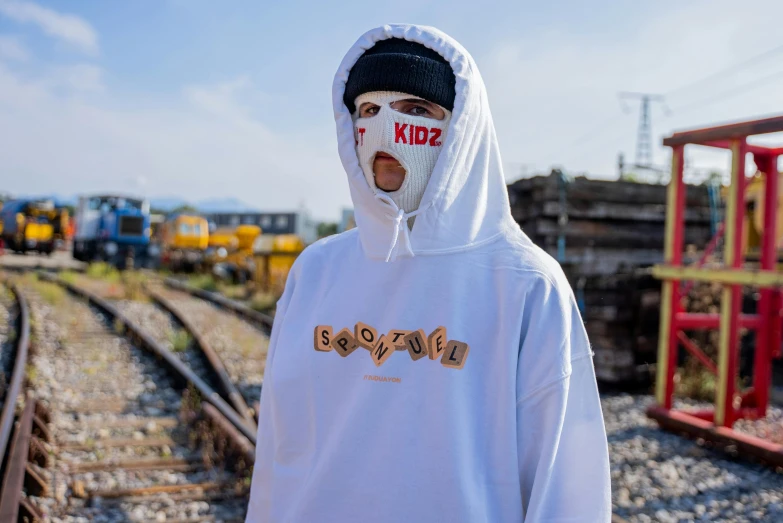 a man wearing a white hoodie standing in front of train tracks, inspired by Károly Brocky, unsplash, graffiti, ski masks, jaeyeon nam, kids, oversized hoodie