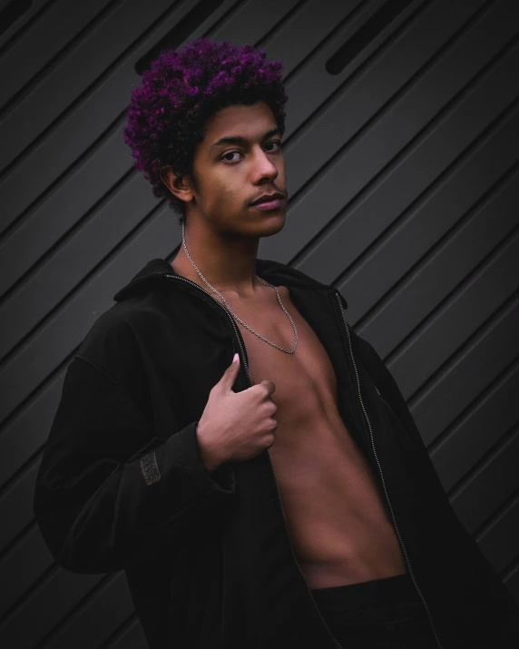 a man in black with purple hair standing by a wall