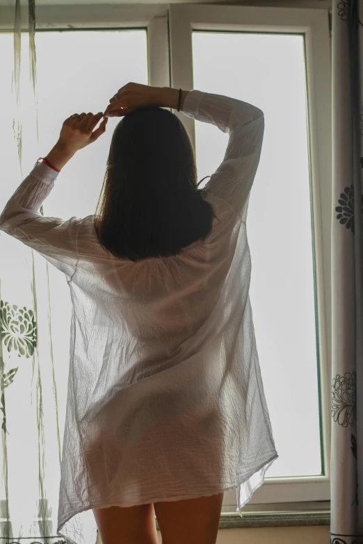 a woman standing in front of a window while looking out the window